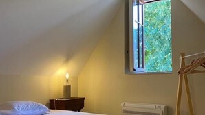 A bedroom with a bed, a nightstand, a lamp, a radiator, and a window with a view of greenery.