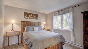 Un dormitorio con una cama de madera, dos lámparas de noche, un ventanal con cortinas y una obra de arte colgada en la pared.