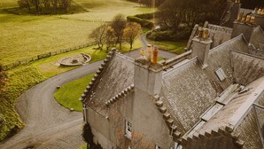 Un château avec une allée sinueuse, une pelouse circulaire aménagée et de nombreuses cheminées.