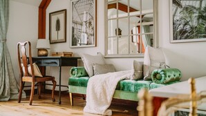 Une pièce chaleureuse avec un canapé vert, une chaise en bois, un bureau et une grande fenêtre donnant sur un immeuble.