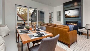 A modern dining area with a wooden table set for two, a leather sofa, and a fireplace. - Abode on Cloud 9, private hot tub, Old Town retreat, groups (Park City)