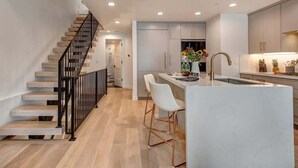A modern kitchen with a central island, white bar stools, and a staircase with black railings. - Abode on Cloud 9, private hot tub, Old Town retreat, groups (Park City)