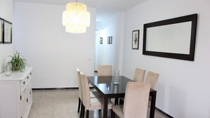 A dining area with a dark wooden table, beige upholstered chairs, a white cabinet, and a hanging light fixture.