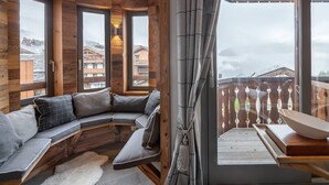 A cozy room with a curved wooden bench, large windows, and a balcony with a wooden railing.