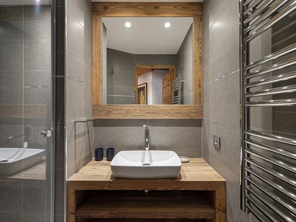Une salle de bain moderne avec un meuble-lavabo en bois, un grand miroir et un porte-serviettes chromé.