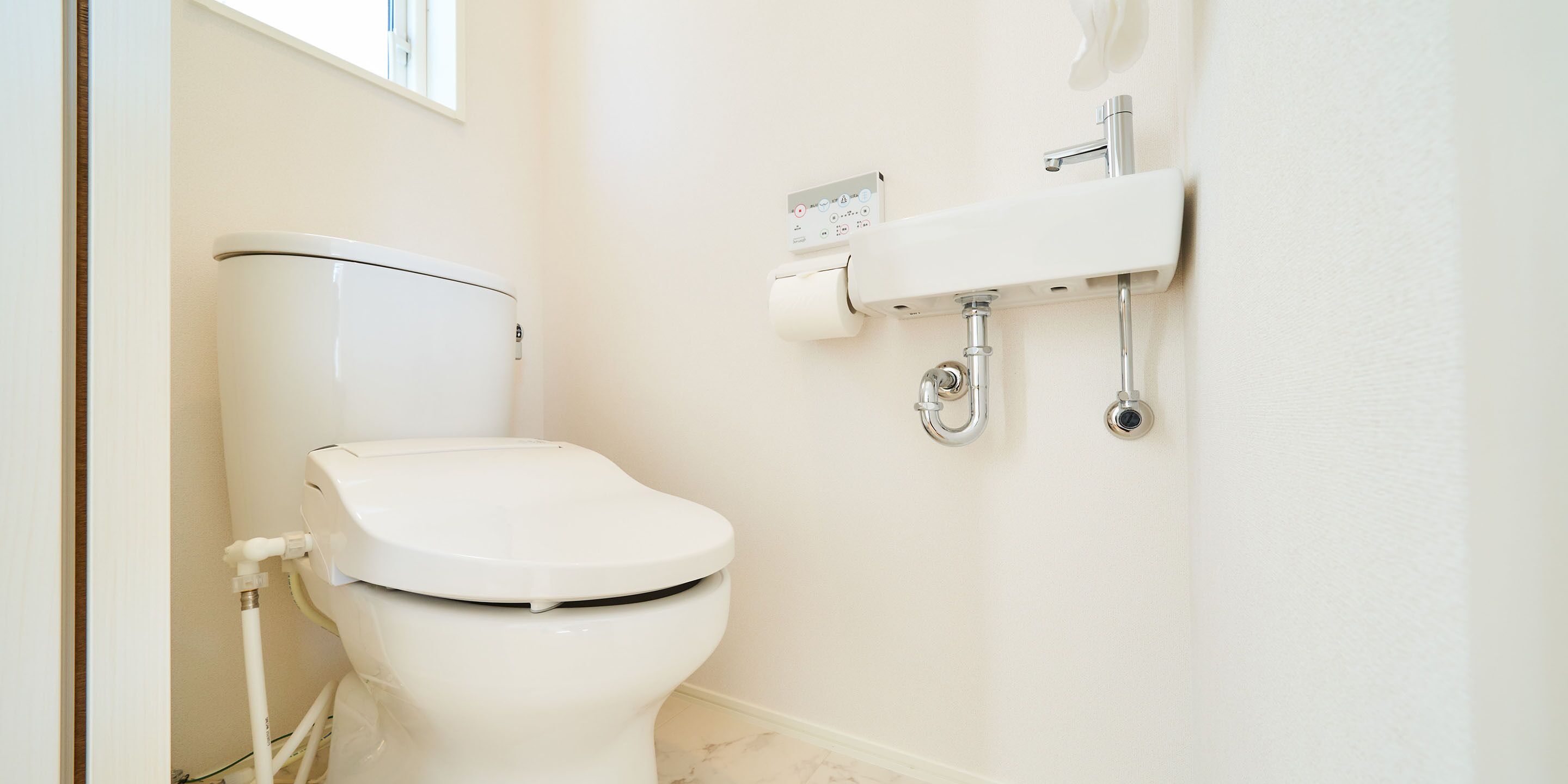 A modern bathroom with a white toilet, a wall-mounted sink, and a toilet paper holder.