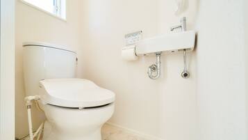 A modern bathroom with a white toilet, a wall-mounted sink, and a toilet paper holder.