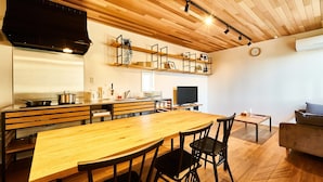 A modern kitchen with wooden cabinets, a large wooden table, and chairs. There is a sofa and a small table in the living area. - Rakuten STAY HOUSE WILL STYLE Saga Imari (Imari)