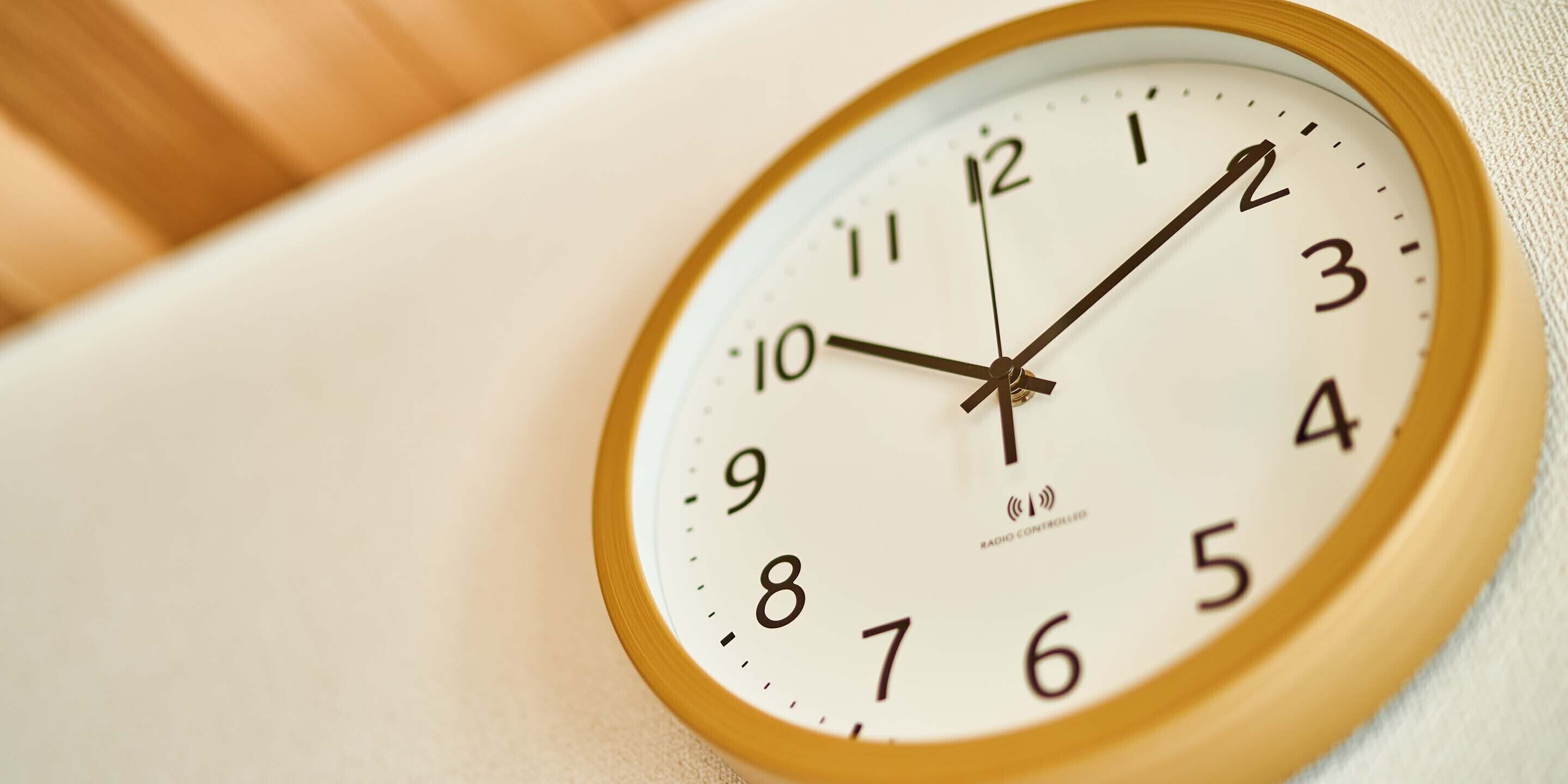 Um relógio analógico fixado na parede, com mostrador branco e moldura de madeira.