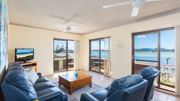 Een woonkamer met een televisie, leren banken, een salontafel en een balkon met uitzicht op zee.