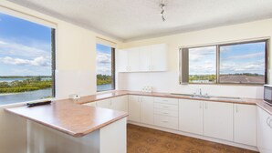Een keuken met witte kastjes, een bruin aanrechtblad en uitzicht op een rivier en groen.