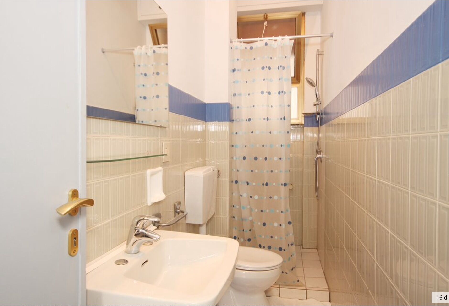 Un baño con lavamanos, inodoro y zona de ducha, con azulejos azules y blancos y una cortina de ducha con lunares.