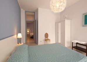 Une chambre à coucher comprenant un lit, une chaise, une armoire, une table de chevet, une lampe et un luminaire au plafond.