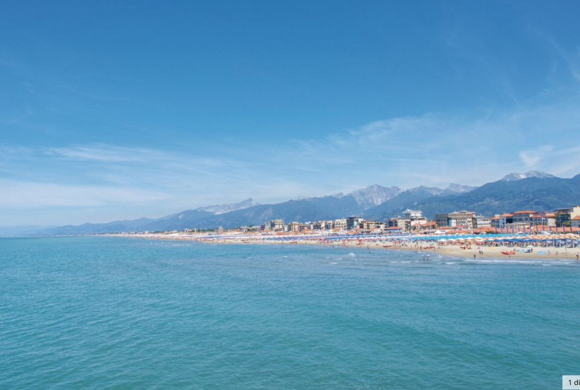 A coastal cityscape with a beach, buildings, and mountains in the background.