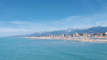 Paesaggio costiero con spiaggia, edifici e montagne sullo sfondo.