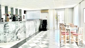 A hotel lobby with a marble reception desk, check-in counter, and a dining area with wooden chairs and a white table. - Eleana Hotel by GHH (Zakynthos)