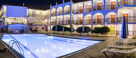 A multi-story hotel with a swimming pool, outdoor seating, and a well-lit facade.