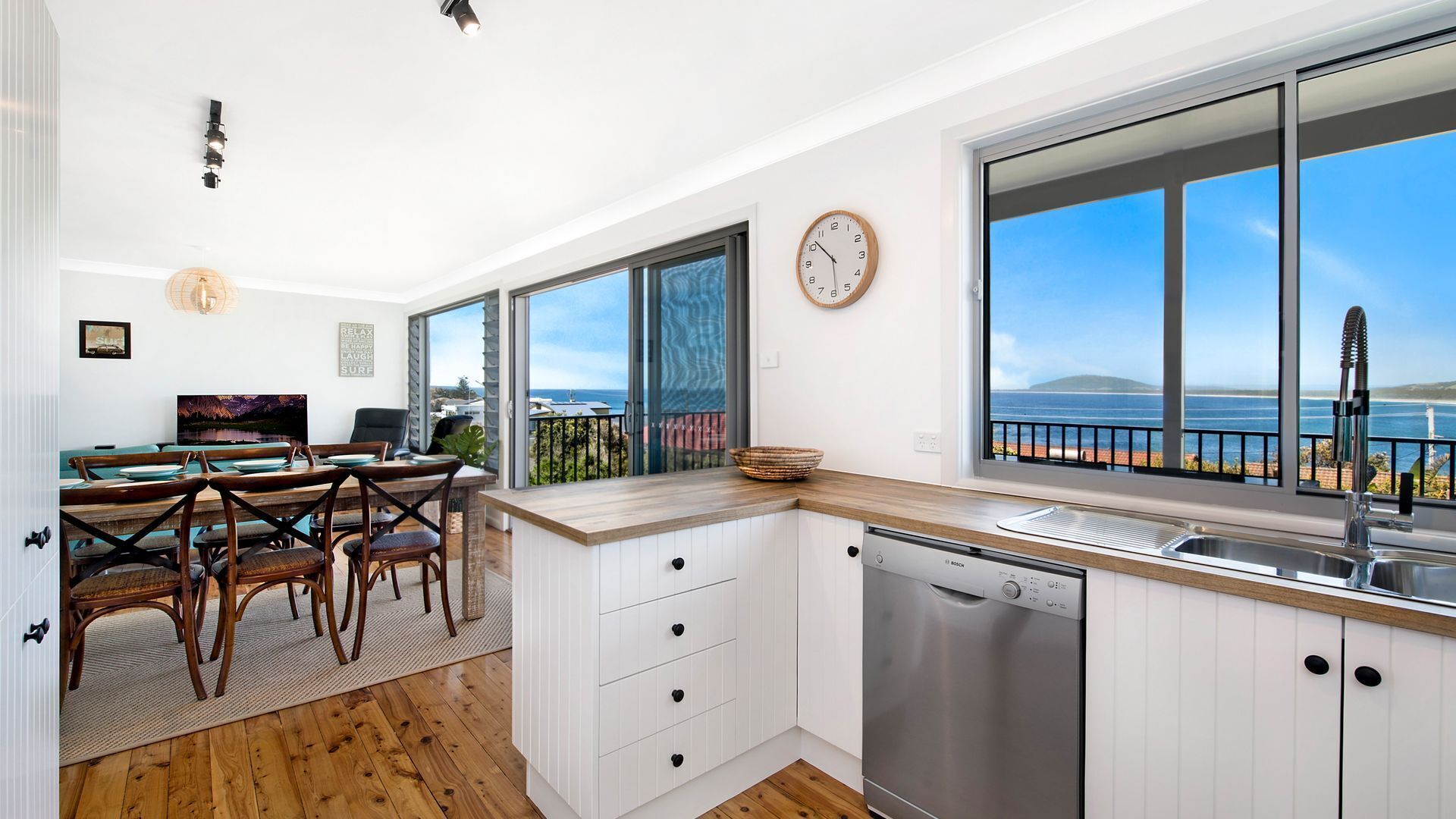 A modern kitchen with wooden cabinets, a Bosch dishwasher, and a large window overlooking the sea.