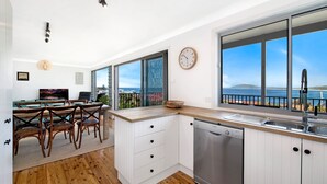 A modern kitchen with wooden cabinets, a Bosch dishwasher, and a large window overlooking the sea. - Cool View - Views of Seven Mile Beach (Gerroa)