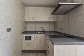 A modern kitchen with light wood cabinets, a built-in microwave, and a stainless steel sink.