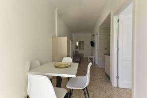 A small, clean room with a dining table, chairs, a bed, and a TV.