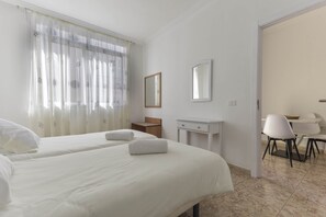 A hotel room with two beds, a small desk, a chair, and a dining area.