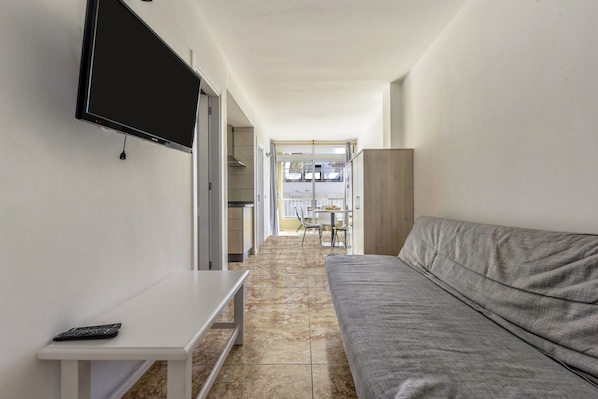 A narrow hallway with a grey sofa, a white table, and a TV mounted on the wall.