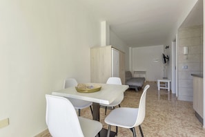 A dining area with a table and chairs, a bed, a small table, and a cabinet.