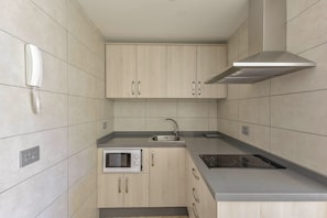 A modern kitchen with light wood cabinets, a built-in microwave, a stainless steel sink, and a gas stove.