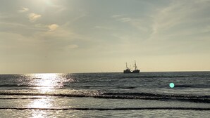 Mare calmo con una nave all'orizzonte e un sole splendente che si riflette sull'acqua.