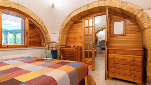 A bedroom with a checkered bedspread, wooden furniture, and arched stone walls.