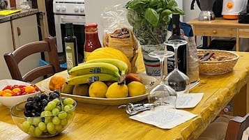 A kitchen with a wooden table set for a meal, featuring fruits, vegetables, and condiments.