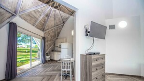 A room with a herringbone floor, a wooden ceiling, a TV mounted on the wall, and a view of a green landscape through the window. - STUDIO 05 - Lake Sumner (Clermont)
