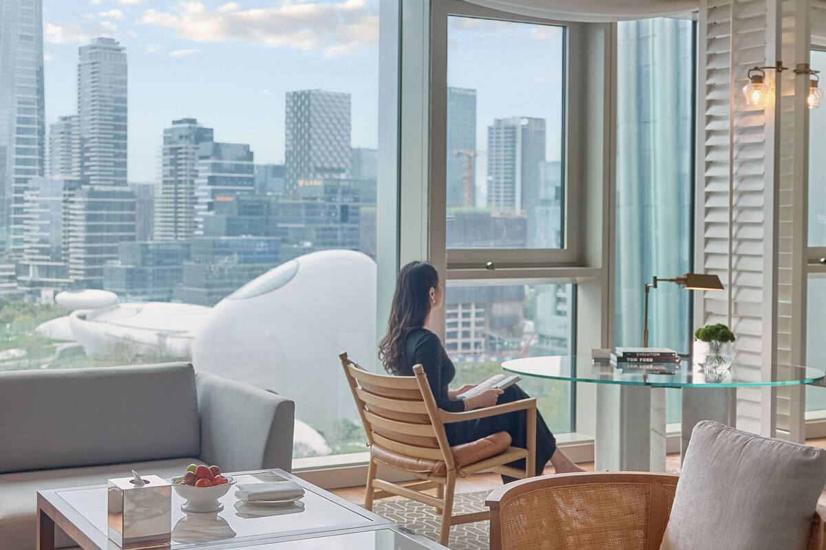 A modern living room with a large window offering a city view, a glass coffee table, and a comfortable seating area.