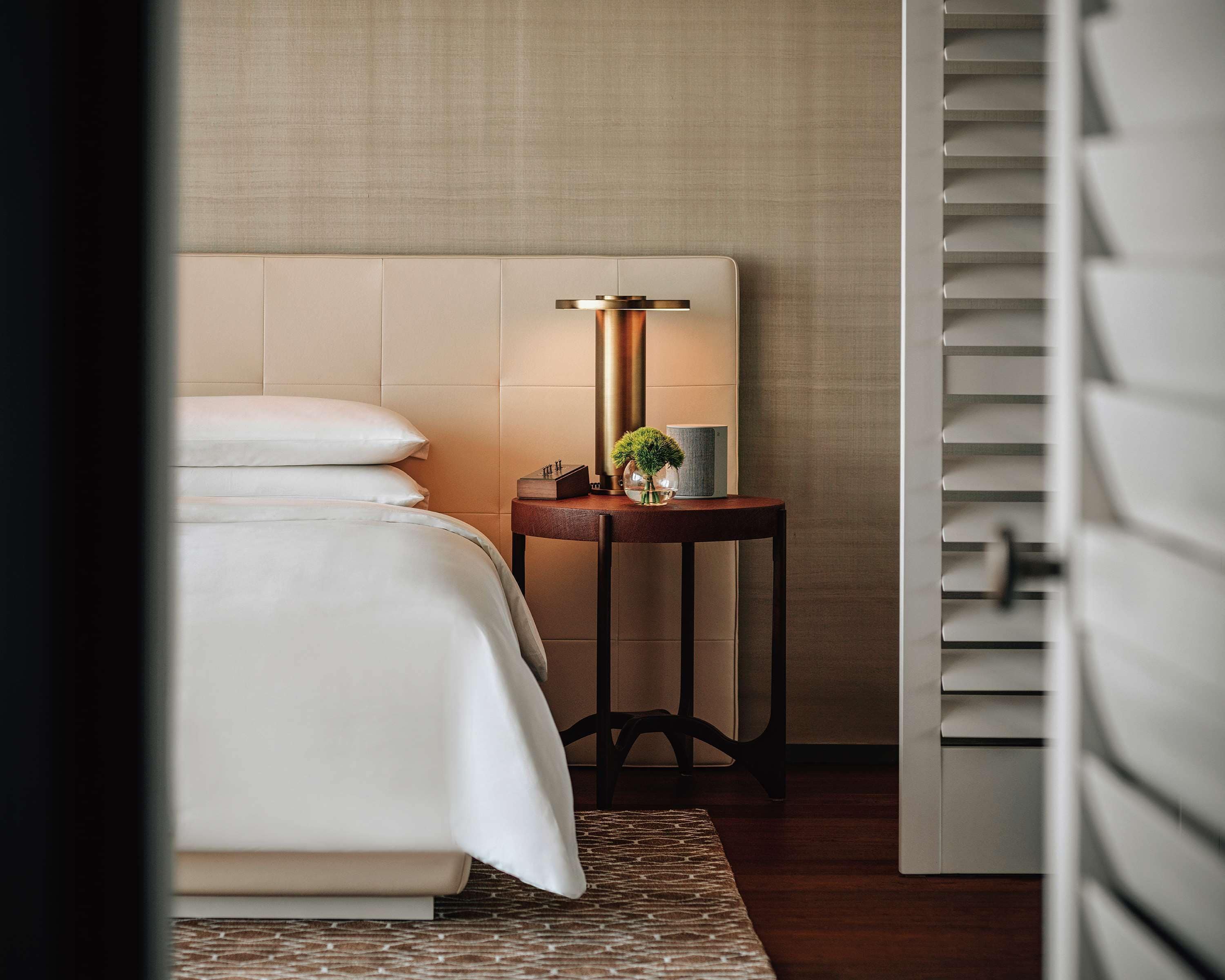 A neatly made bed with white linens, a bedside table with a lamp, and a small potted plant.
