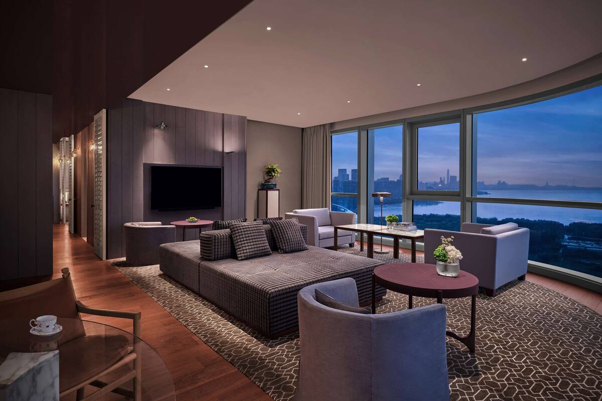 A modern living room with a large TV, comfortable seating, a dining area, and a view of the city skyline.