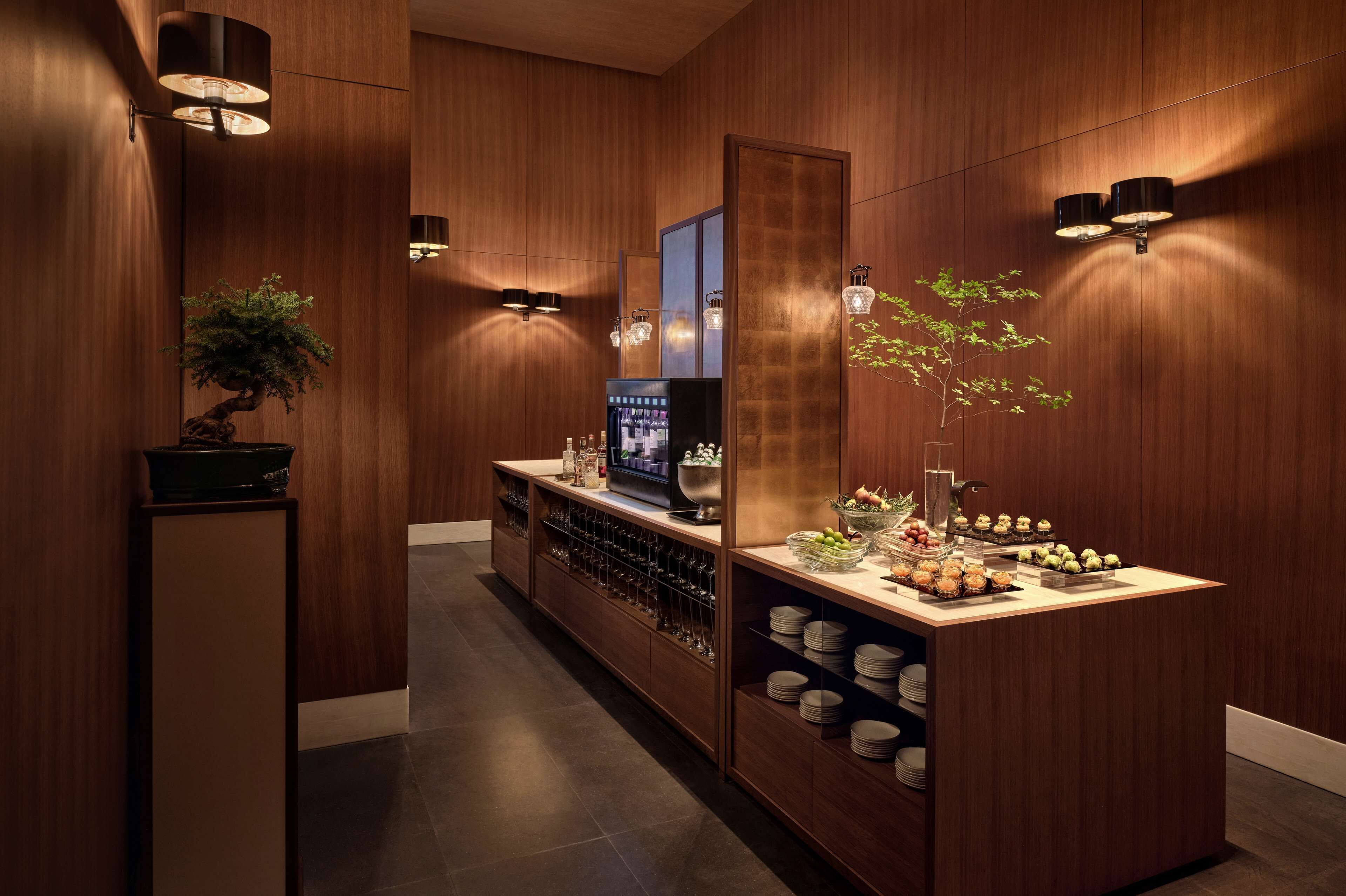 Um hall de hotel moderno com uma mesa de recepção de madeira, uma televisão e uma área de buffet com diversos alimentos.