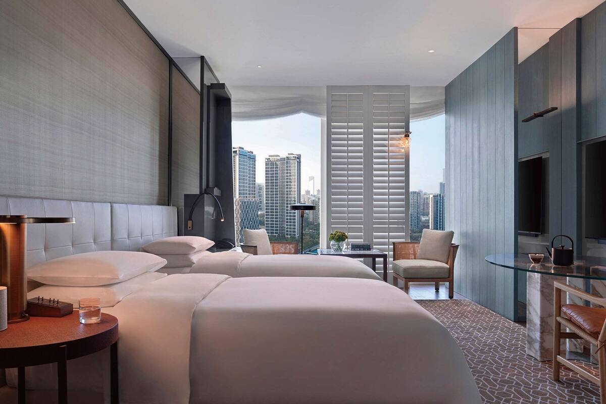 A modern hotel room with a large bed, a small table, a chair, and a TV.