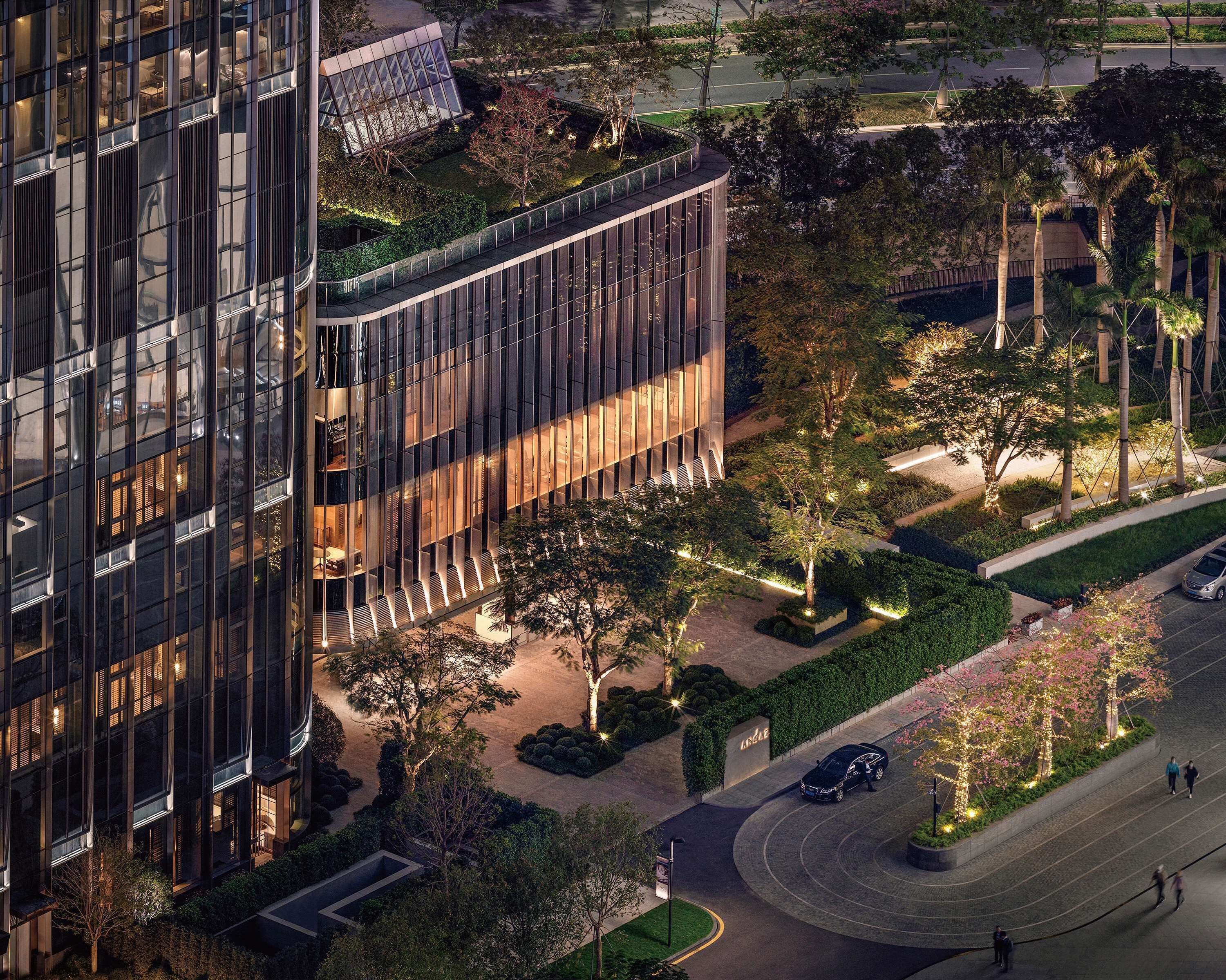 A modern building with a glass facade, surrounded by landscaped gardens and trees.