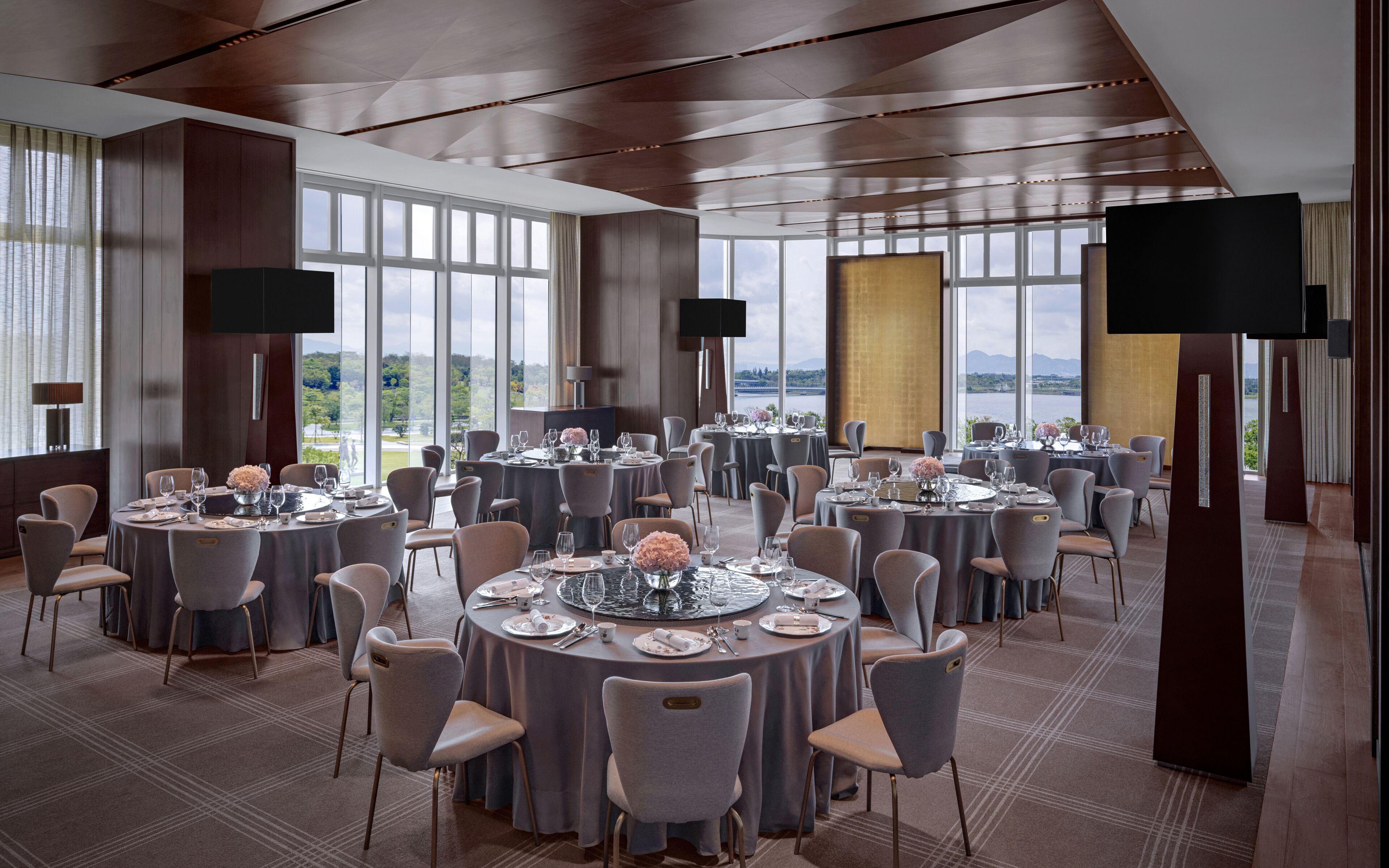 Un comedor espacioso con varias mesas redondas, sillas grises tapizadas y ventanas amplias que ofrecen vistas al exterior.