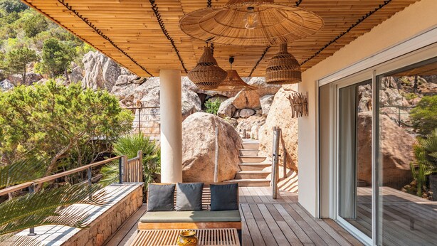 A wooden deck with a sofa and a table, surrounded by large rocks and trees. - Villa Elsa Di Palombaggia (Porto-Vecchio)