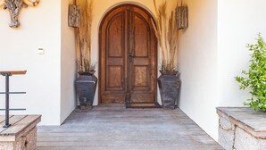 A wooden double door with a rustic design, flanked by two large planters with tall grasses. - Villa Elsa Di Palombaggia (Porto-Vecchio)