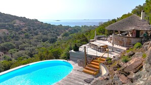 A poolside area with a view of the sea, a wooden deck, and a bar area. - Villa Elsa Di Palombaggia (Porto-Vecchio)