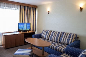 A hotel room with a sofa, a small table, a television, and a cabinet.