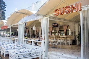 An outdoor sushi restaurant with white furniture and a covered seating area.