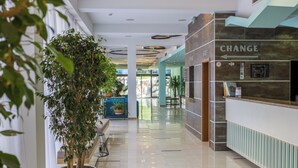 A modern lobby with a reception desk, a large potted tree, and a sign indicating a change. - Kuban Resort and Aquapark (Nessebar)