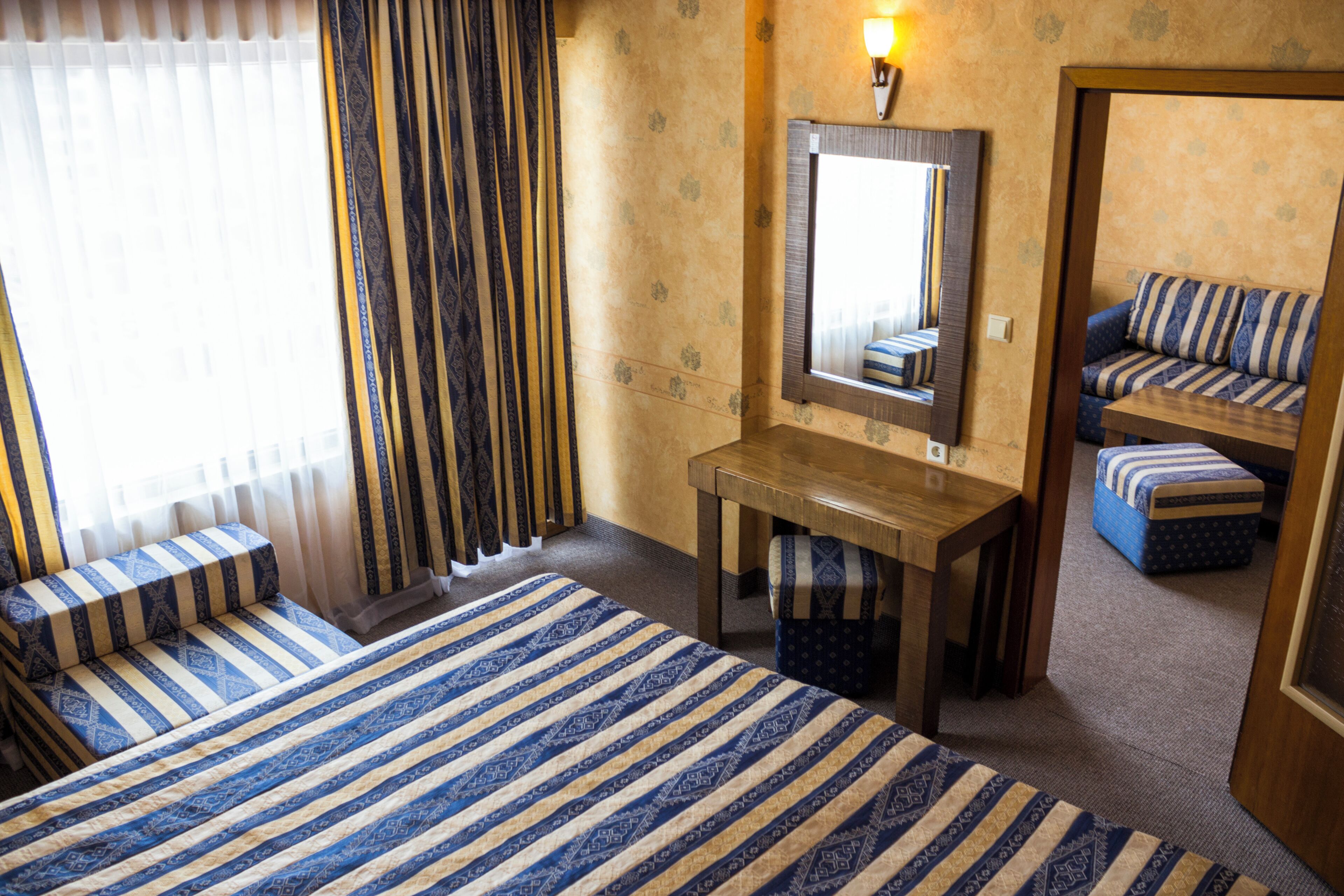 Een hotelkamer met een bed, een bureau, een stoel, een spiegel en een raam met gordijnen.
