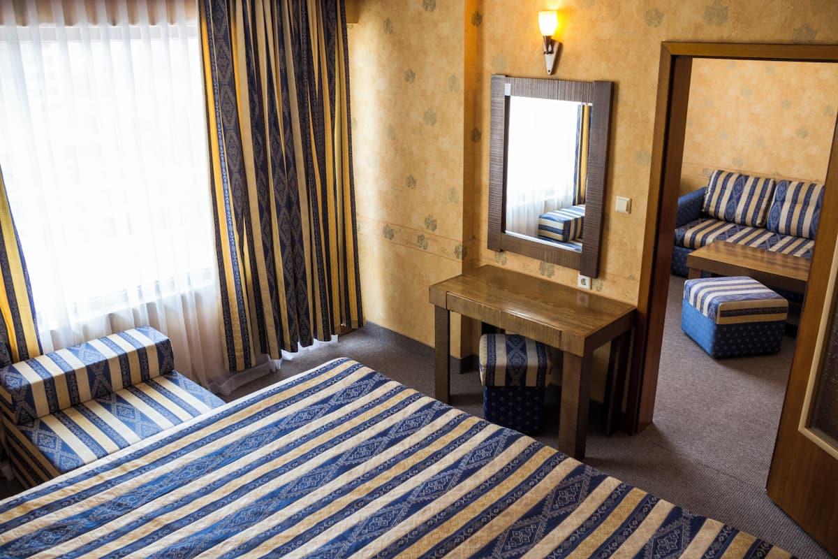 Een hotelkamer met een bed, een bureau, een stoel, een spiegel en een raam met gordijnen.