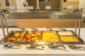 Buffet com diversas opções de comida e utensílios para servir.