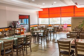Un restaurante con varias mesas y sillas, una barra con caja registradora y una ventana con persianas naranjas.
